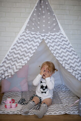 Adorable beautiful happy smiling ginger-haired toddler little girl is playing peekaboo sitting in a teepee wigwam © Tina
