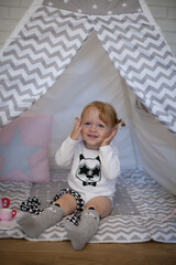 Adorable beautiful happy smiling ginger-haired toddler little girl is playing peekaboo sitting in a teepee wigwam © Tina