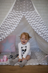Adorable beautiful happy smiling ginger-haired toddler little girl is playing with her toys sitting in a teepee wigwam © Tina