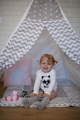 Adorable beautiful happy smiling ginger-haired toddler little girl is playing with her toys sitting in a teepee wigwam © Tina