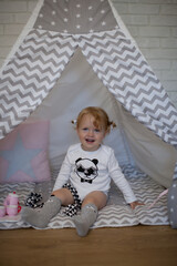 Adorable beautiful happy smiling ginger-haired toddler little girl is playing with her toys sitting in a teepee wigwam © Tina