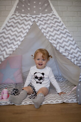 Adorable beautiful happy smiling ginger-haired toddler little girl is playing with her toys sitting in a teepee wigwam © Tina