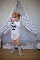 Adorable beautiful happy smiling ginger-haired toddler little girl is playing with her toys and drinking tea standing at the teepee wigwam © Tina