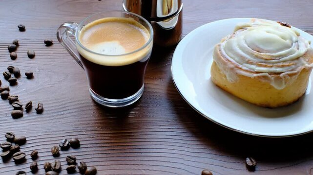 Cinnamon roll on a plate on a wooden background with a glass of espresso next to it