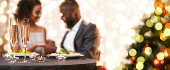 Glasses of champagne and candles on restaurant table, black couple in love having romantic date