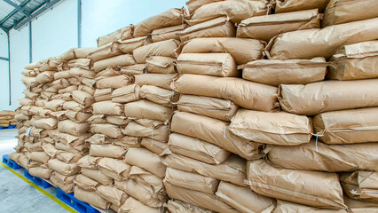 Stacks of large brown paper bags are neatly piled on pallets inside a warehouse, suggesting storage or inventory of goods in an industrial setting