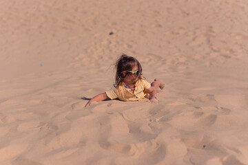 Beautiful little girl in a yellow dress and sunglasses posing on sand dunes. Sunny summer day, beautiful big sand dunes and little girl alone in desert