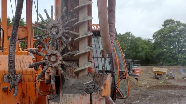Industrial piling auger drilling rig in action under cloudy sky at a construction site