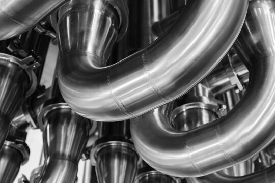 A series of pipes are shown in a close up. The pipes are silver and appear to be connected to one another. Concept of industrial machinery and the importance of the pipes in the process
