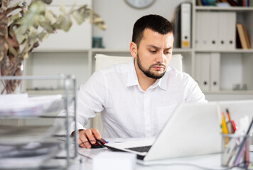 Obraz premium Man office worker sitting at desk and using laptop during his workday.