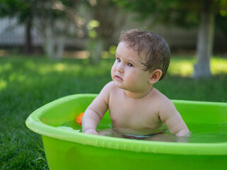 Cute baby boy bathes in a basin outdoors in summer.
