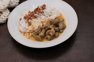 Gulai Kambing or Lamb Curry with rice on a white palte and krupuk, Traditional Javanese mutton curry soup.