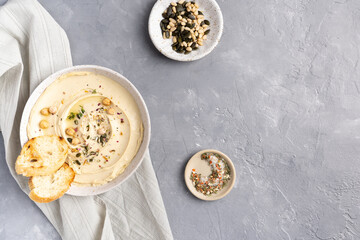 Hummus with olive oil in a gray ceramic plate. Toast and breadsticks for snacks. Top view, on a gray background.