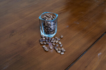 Sattered coffee beans and glass of coffee beans on wooden table, making coffee homemade.