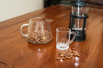 Brewing method French press coffee maker, with beans on coffee server pot, french press, glass and Scattered coffee beans on the wooden table, making coffee homemade.