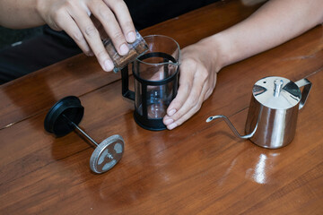 Close up of a person's hands pouring coffee powder in a black french press on the wooden table, Brewing a Coffee in a French Press at home.