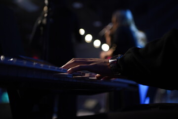 A striking close-up of a Black man's hands gracefully dancing over a keyboard, illuminated by cinematic lighting. The dark, moody atmosphere, combined with backlighting and a blurred background, creat