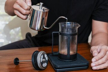 Closeup a hand Pouring the hot water into coffee powder on the french press glass, Brewing method French press coffee maker.