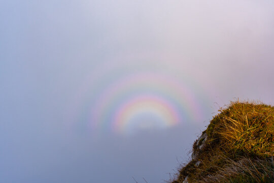 Mysterious fog and rainbow on a cloud over a grassy hillside on a misty morning. Concept of natural phenomena, atmospheric optics and serene landscape in nature. High quality photo