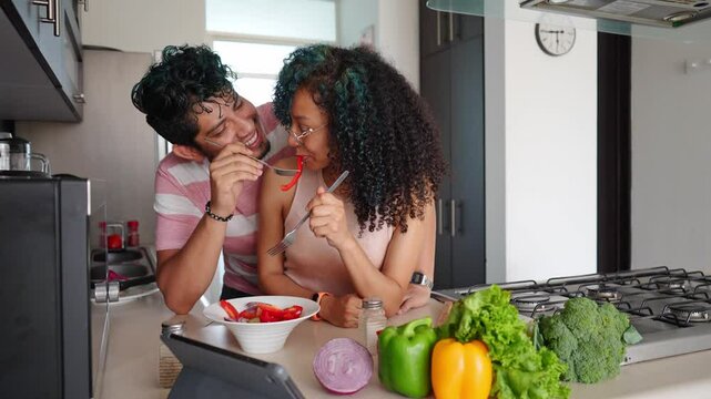 loving young couple eating salad in the kitchen, african american wife giving food to her hispanic husband