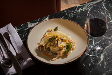 A plate of Chicken Alfredo Tagliatelle with a glass of red wine. Luxurious and expensive gourmet meal prepared on a black marble table, served with a glass of wine