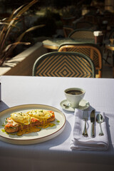 A wonderful breakfast prepared with a plate of Eggs Benedicts and a cup of coffee. Breakfast prepared and served in a beautiful restaurant, food.