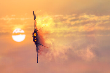 A military jet on its side fires the engines leaving a vapor trail in its wake