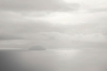 Obraz premium A Small Boat Navigates a Foggy Sea with a Single Island in the Distance