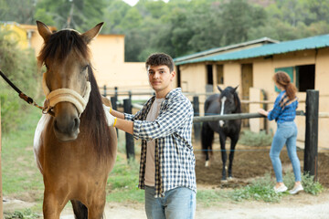 Young owner man washing and brushing horse in backyard of small farm