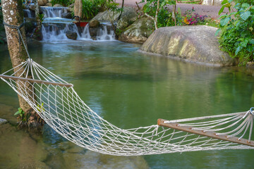 A peaceful hammock by a serene stream in nature, surrounded by lush greenery with sunlight filtering through the trees. The gentle stream flows beside the hammock, creating a calm and tranquil atmosph