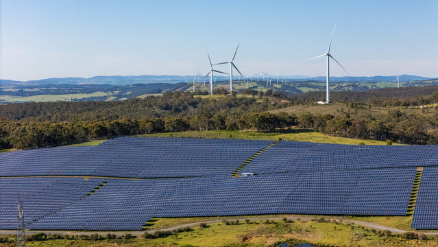Aerial drone view of a hybrid solar and wind farm showing the large wind turbines in the background for renewable clean energy supply located at Bannister, NSW, Australia on a sunny day