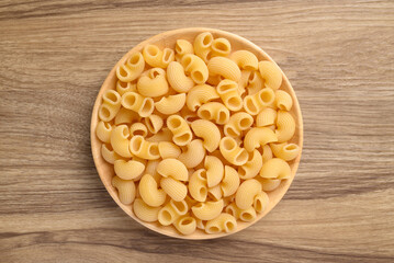 Raw macaroni pasta in bowl on wooden background, Food ingredient, Table top view