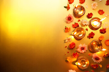 Diwali celebration. Diya lamps and beautiful flowers on golden background, flat lay. Space for text