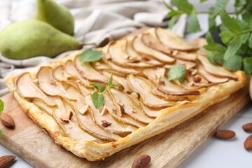 Delicious puff pastry tart with pears, almond and mint on light table, closeup