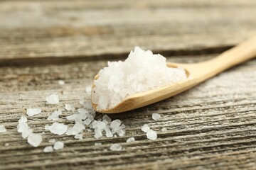 Sea salt in spoon on wooden table, closeup