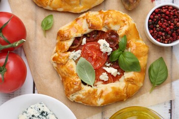 Tasty galettes with tomato, basil and cheese on white wooden table, flat lay
