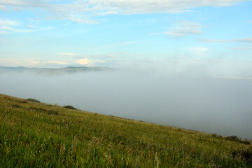 View from the top of the hill to the valley covered with dense and dense fog on a sunny summer morning.