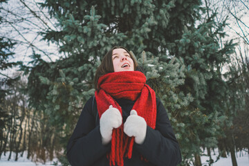 A smiling woman with a red scarf enjoys a snowy winter day in a serene forest setting beneath a...