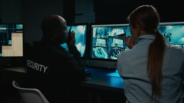 Medium rear shot of diverse team of security guards discussing potential dangerous incident while monitoring CCTV footage, Caucasian woman pointing to screen, black man reporting on portable radio