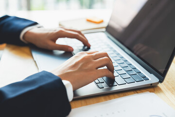 Fototapeta premium Businessman hand typing on laptop and working on computer on wooden table.