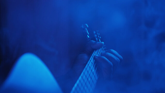 Acoustic concert. Guitar player. Pop event. Music stage performer man hands improvising with chords on string instrument at night show in neon blue smoke.