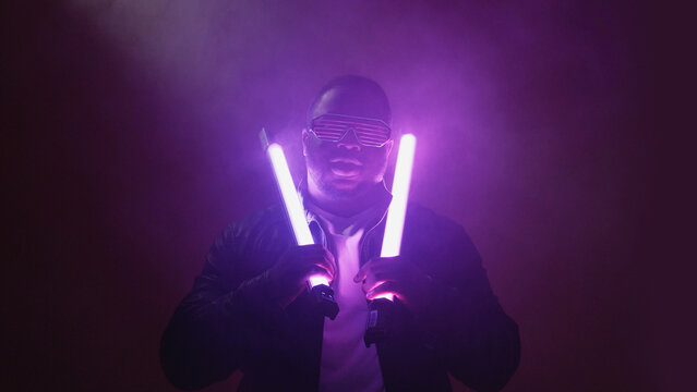 Rap show. Nightclub performance. Cool stylish confident joyful man in trendy sunglasses at hip hop event stage on bright neon lamp light purple smoke background.
