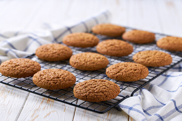 Freshly baked oatmeal cookies cooling on a black wire rack, with in a light kitchen table, selective focus.