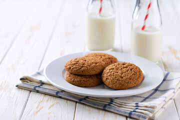 Bottles with fresh milk and oatmeal cookies on a on a white table, selective focus.