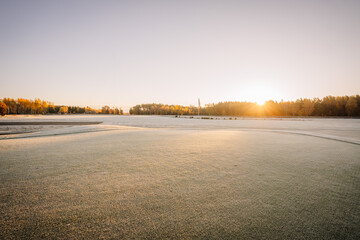 A wide, frost-covered golf course at sunrise, with golden light illuminating the distant trees and...