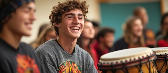 A young man with curly hair smiles while sitting in a group of people playing drums.