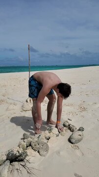 Young man stacking stones and coral reef dead to build a castle on seashore, cayo de agua caribbean island, Los Roques Archipelago