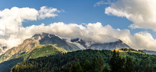 Tops of Alps mountains in clouds with sky, green forest on the france normal way to top of Mont Blanc