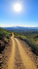 Naklejka premium Scenic Desert Trail Beneath a Bright Sun with Mountain Views in the Distance