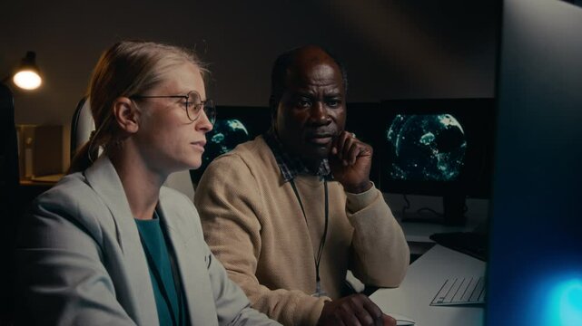 Medium shot of two diverse cyber security specialists, African American man, Caucasian woman in glasses, studying computer code together, discussing bug, senior colleague helping junior team member - Powered by Adobe